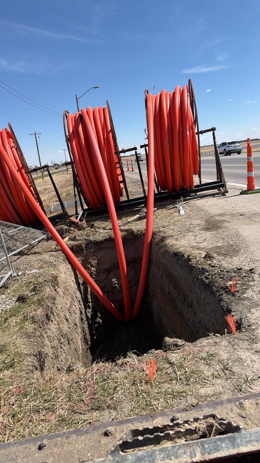 utility-conduit-trench-excavation-installation Thick orange utility conduit lines feeding down into a deep excavated trench from continuous storage reels on a civil construction site.