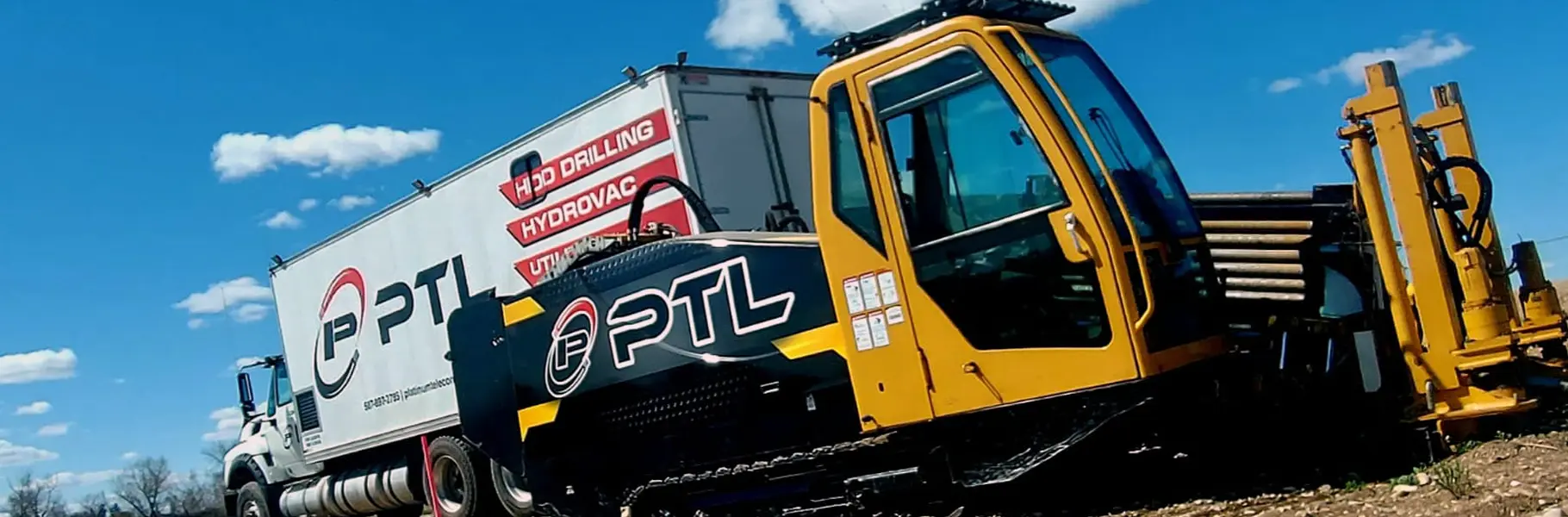 Yellow directional drilling rig and a white utility support truck staged side-by-side on an outdoor construction site under a blue sky with scattered clouds.