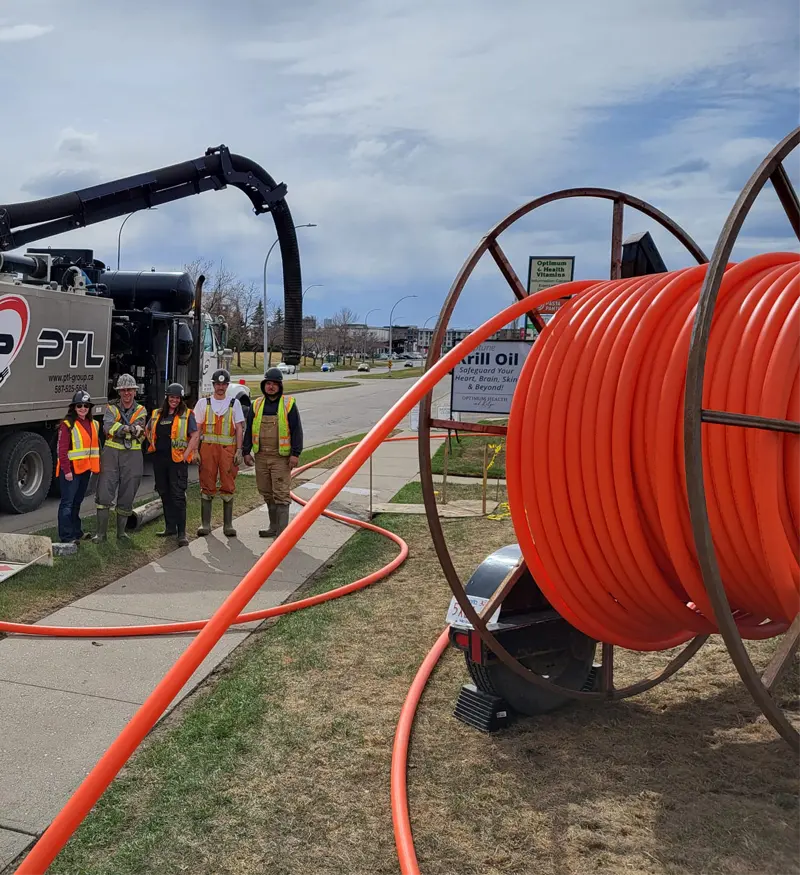 utility-conduit-installation-hydrovac-truck Large reel of orange underground utility conduit piping next to a civil infrastructure crew and a high-capacity hydrovac truck on an active job site.