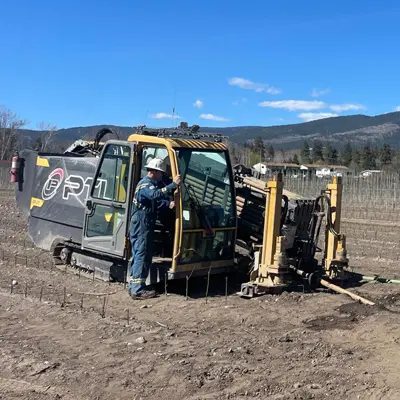 hdd-directional-drill-rig-operator Construction operator standing beside a compact, track-mounted horizontal directional drill rig on an unpaved utility work site.