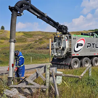An operator in blue coveralls guiding a hydrovac truck boom for precise daylighting excavation on a grassy slope.
