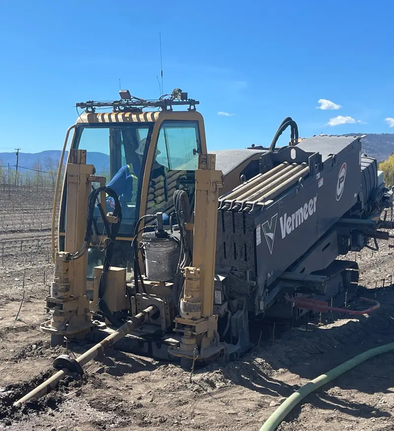 vermeer-hdd-drill-rig-operations Yellow Vermeer horizontal directional drill rig loaded with drill rods on an unpaved path at a trenchless utility construction site.