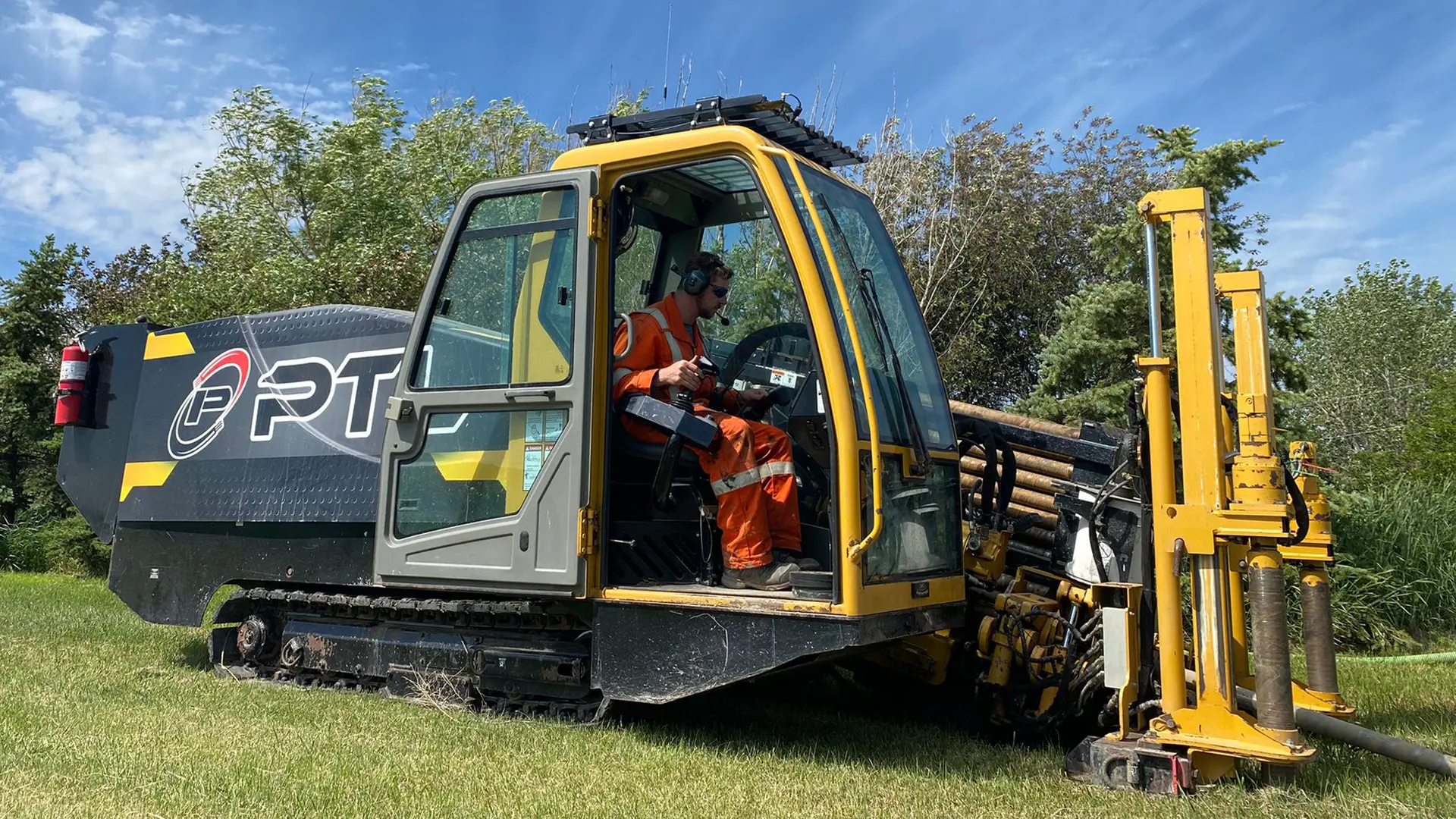 directional-drilling-rig-utility-installation Yellow Vermeer directional boring rig and trenchless pipeline construction crew installing underground utility conduit in a grassy field.