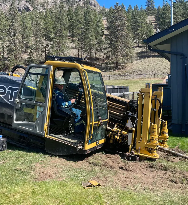 trenchless-pipeline-installation-hdd-drilling Yellow Vermeer directional drill rig with a field operator visible inside the cab executing a trenchless utility installation next to a property line.